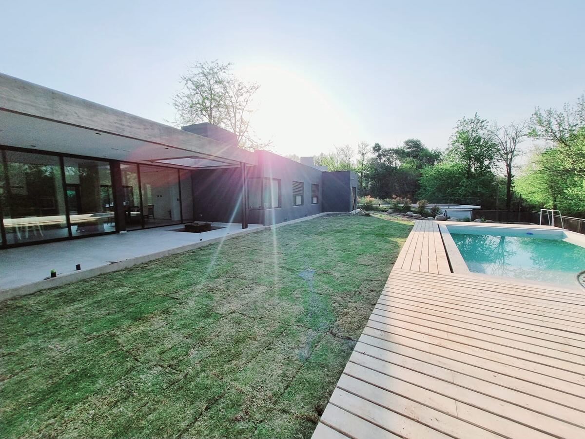 Césped colocado junto a una casa de líneas modernas, una pileta y un deck de madera