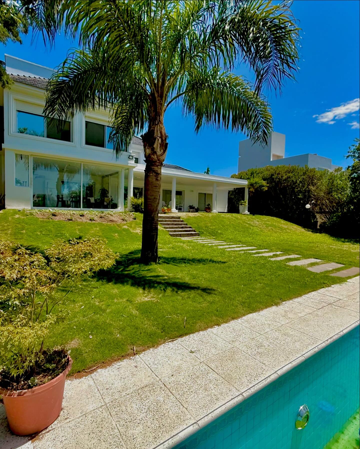 Jardín con césped, palmera, sendero de piedra y pileta frente a una casa en Lomas de la Carolina