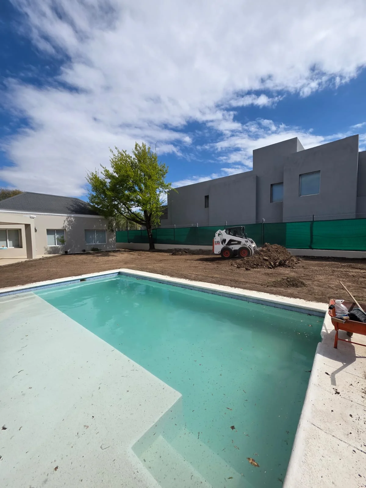 Minicargadora trabajando en la preparación del terreno junto a una pileta, en una obra de Vivero Online